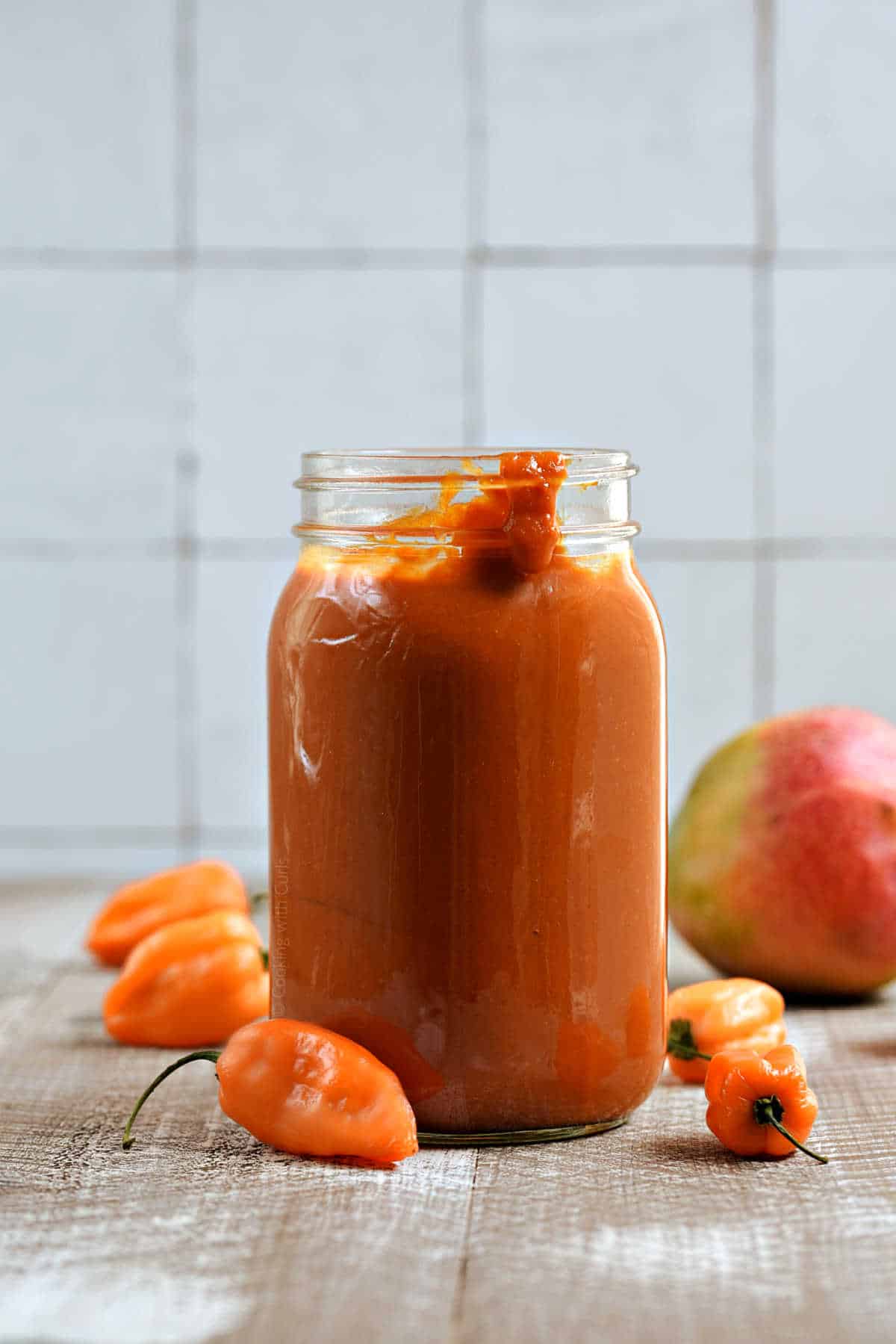 Mango Habanero BBQ Sauce in a mason jar with peppers and a mango in the background.