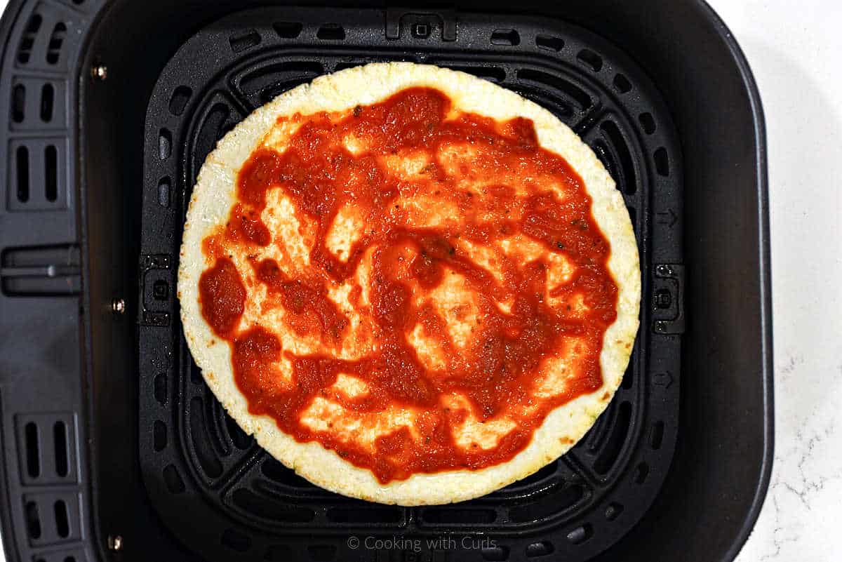 Flour tortilla with pizza sauce in air fryer basket.