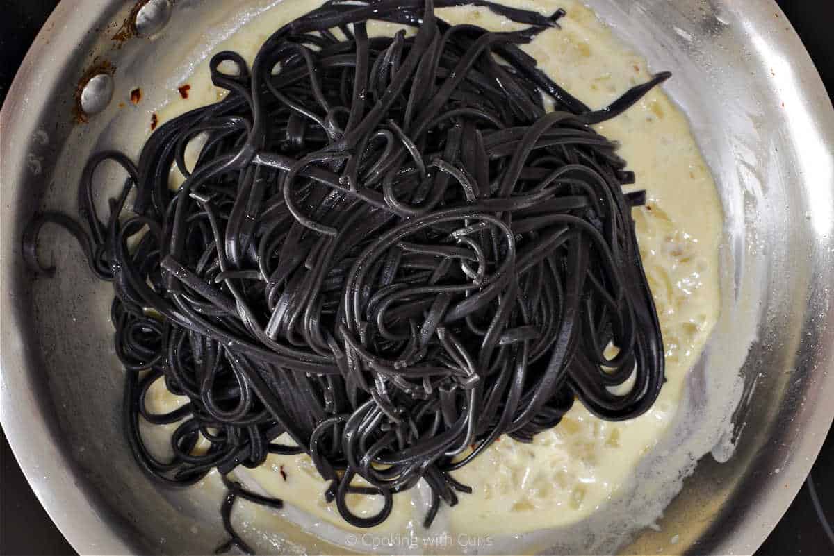 Black pasta added to sauce in skillet.