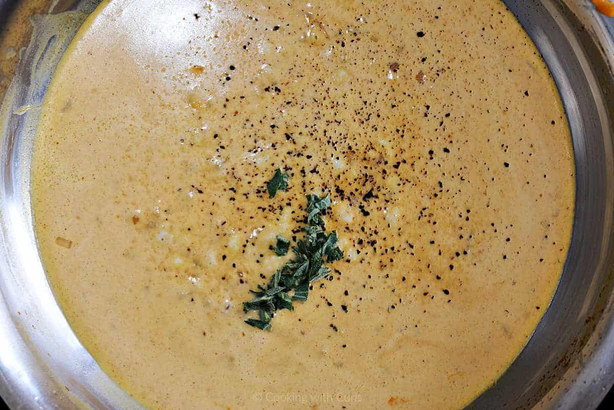 Chopped sage and pepper added to pumpkin sauce in skillet.