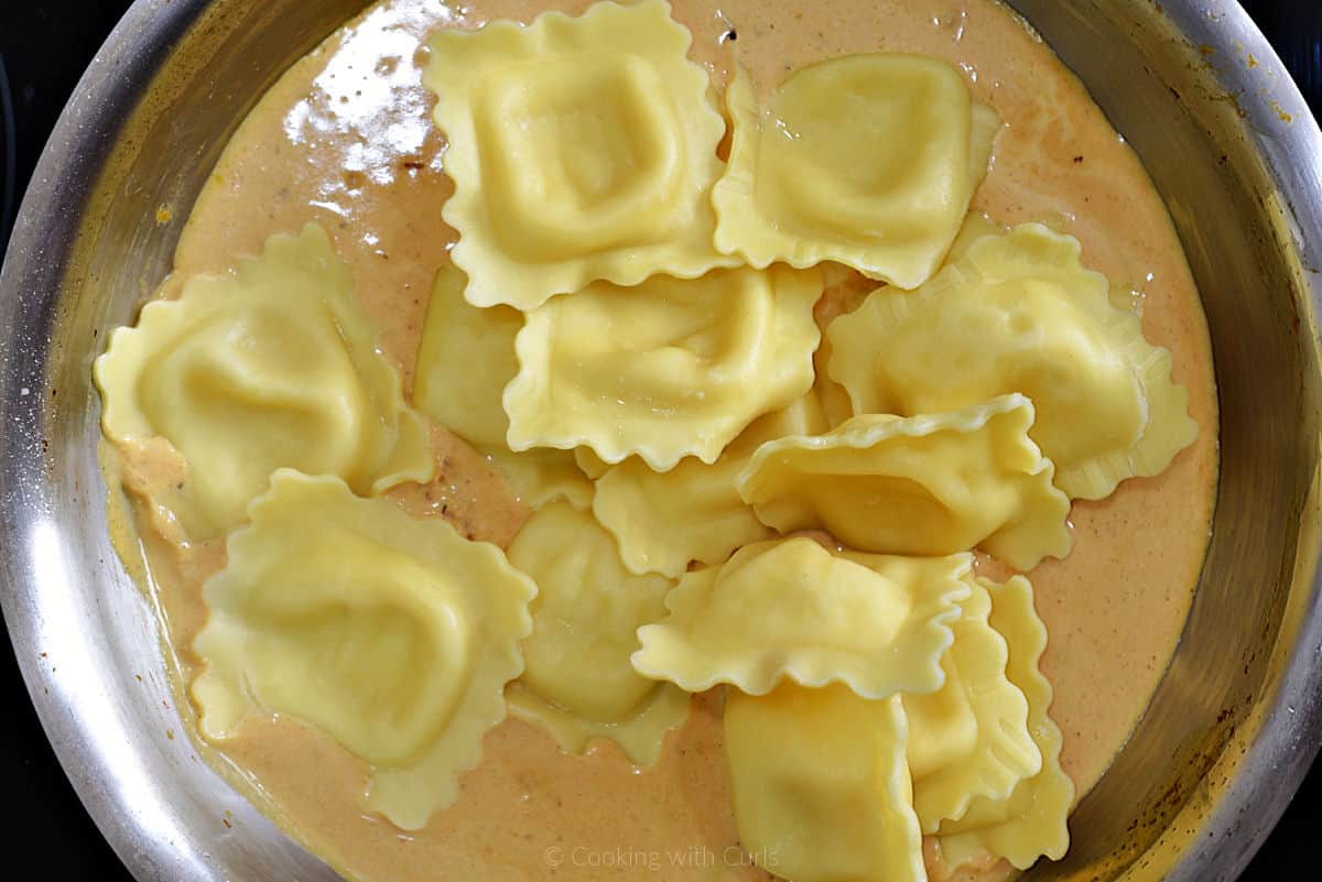 Cooked ravioli added to pumpkin sauce in skillet.