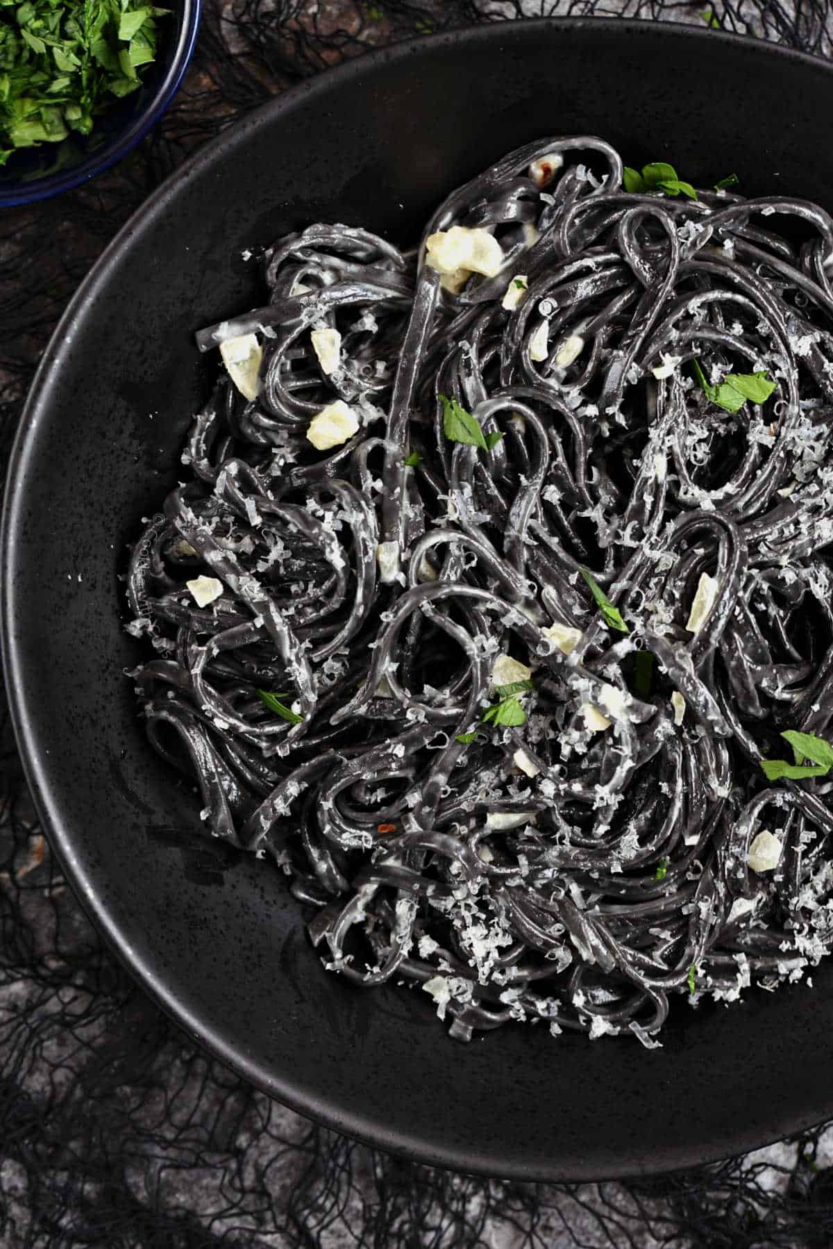 Black pasta swirled around in a black bowl and topped with grated parmesan.