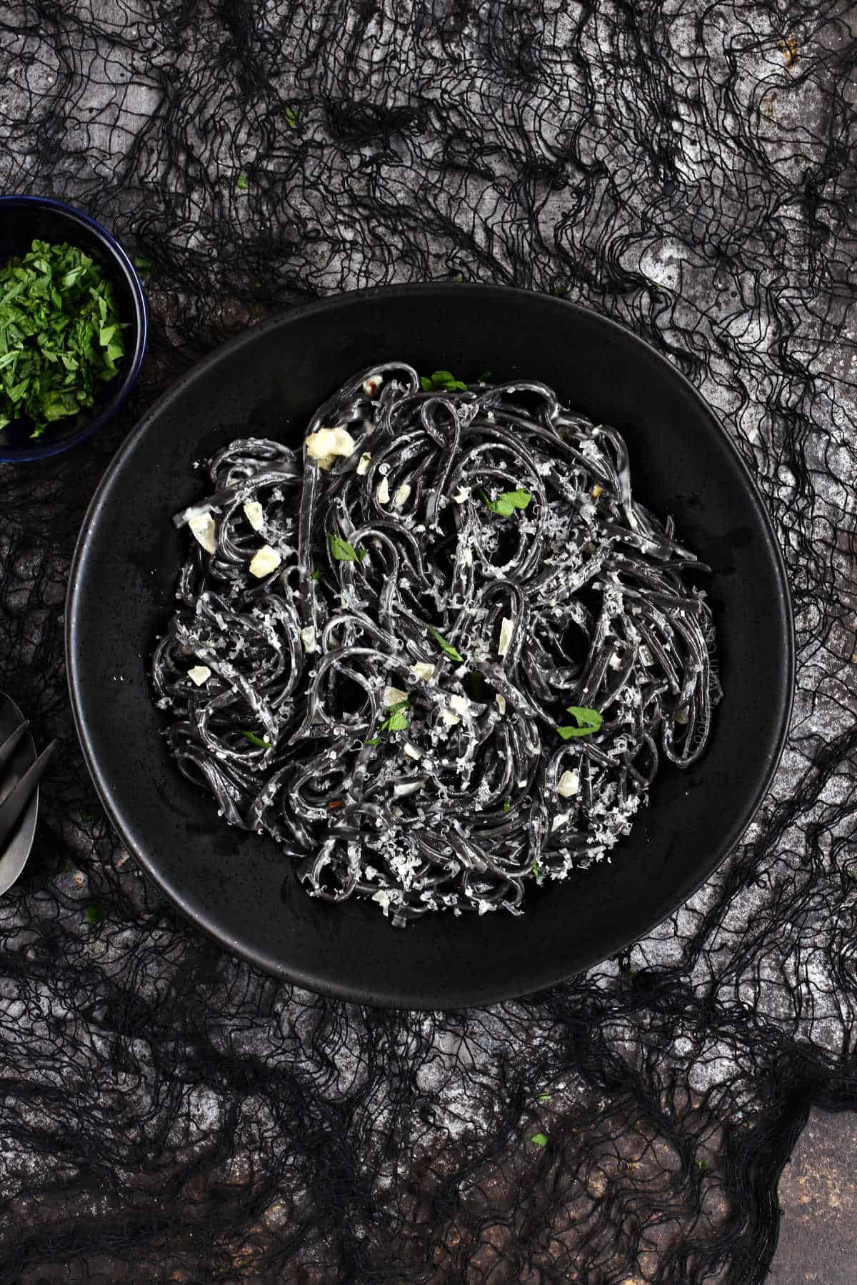 Black swirling pasta with grated parmesan cheese on black spider webbing.