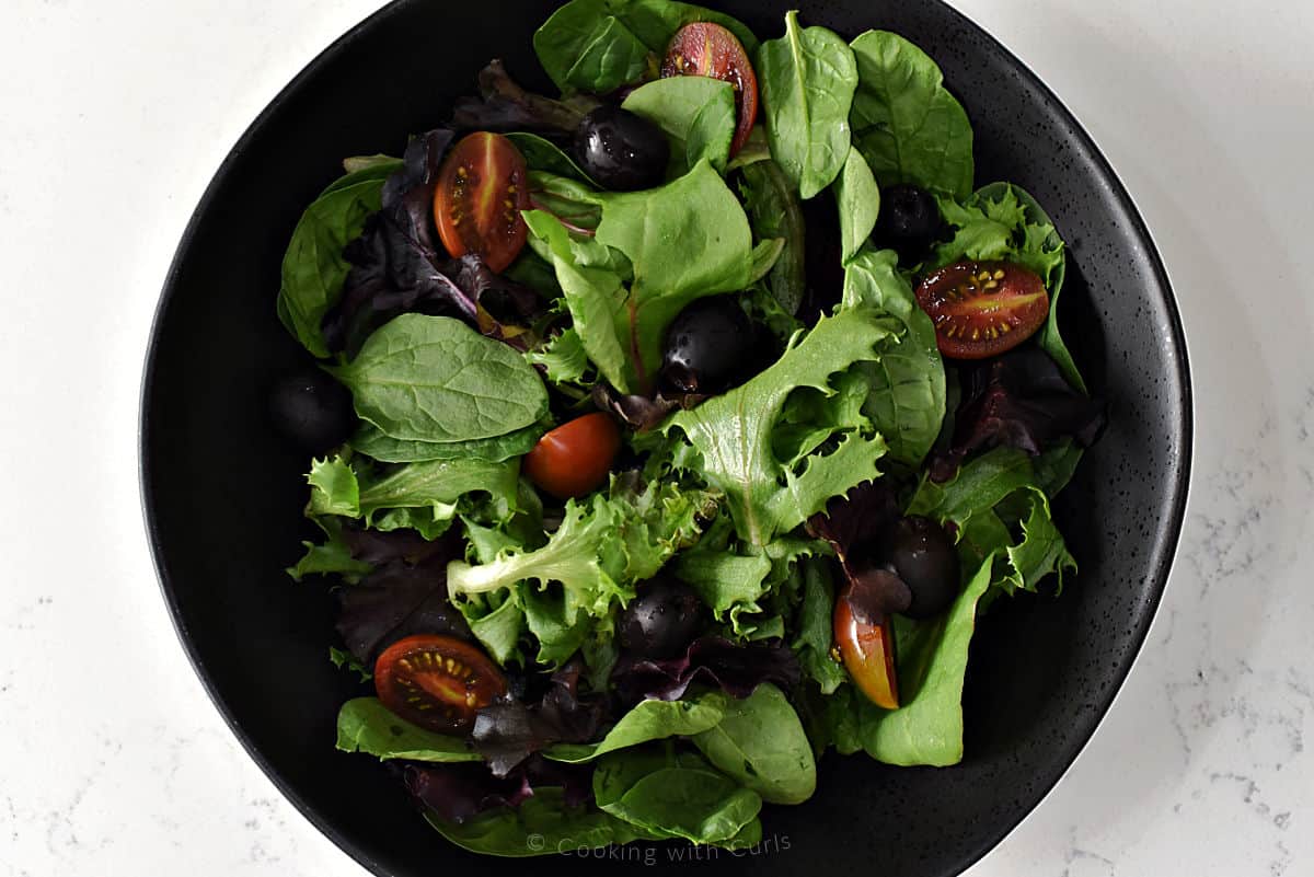 Mixed greens, black olives, and cherry tomatoes in serving bowl.