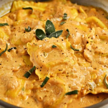 Ravioli covered in creamy pumpkin sauce, sprinkled with fresh sage leaves.