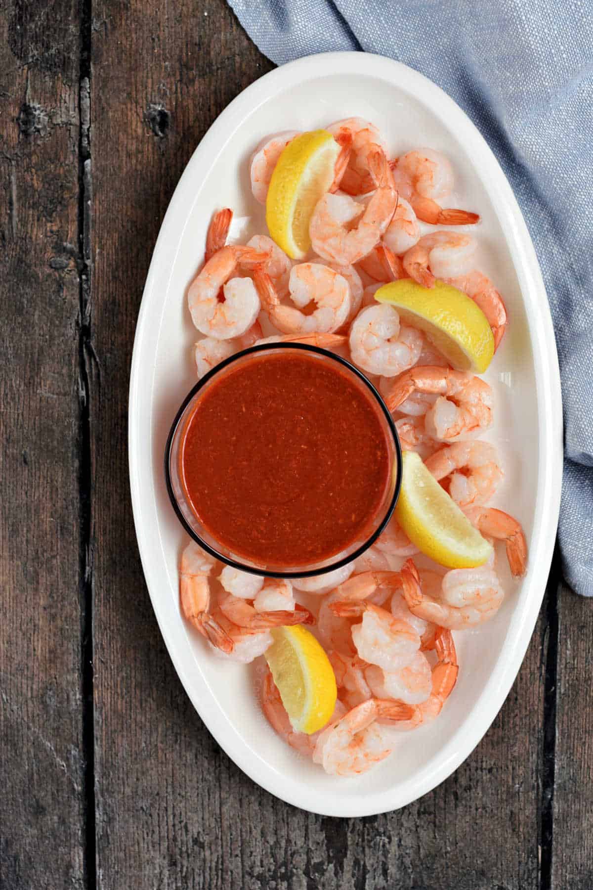 Oval platter topped with cooked shrimp, lemon wedges, and a small bowl of cocktail sauce.