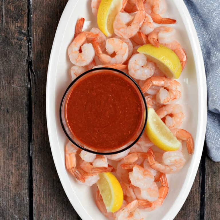 Oval platter topped with cooked shrimp, lemon wedges, and a small bowl of cocktail sauce.