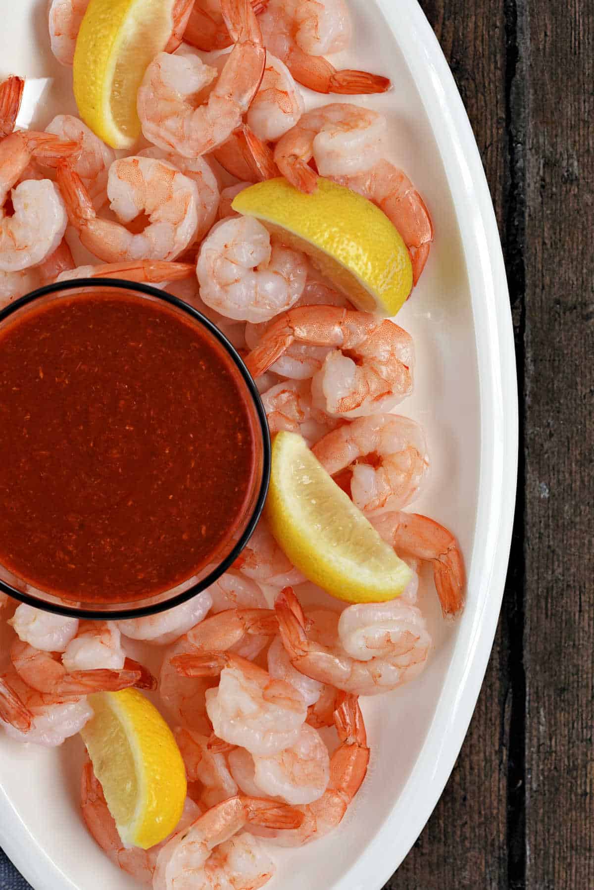 Cooked shrimp, lemon wedges and a small bowl of cocktail sauce on a serving platter.