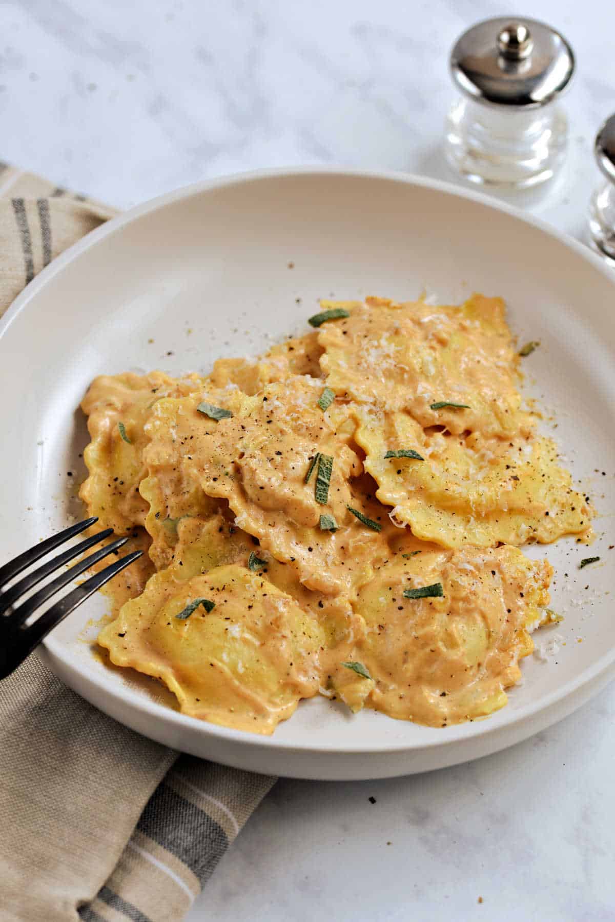 Ravioli with pumpkin sauce on a plate sprinkled with sage and pepper.