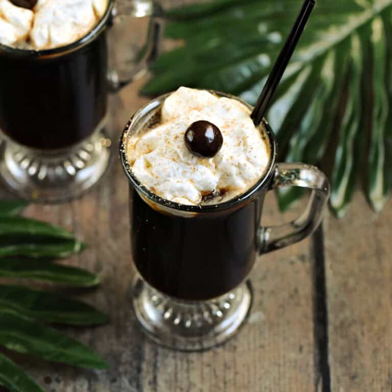 Two glass mugs filled with a coffee cocktail topped with whipped cream and a chocolate covered coffee bean.