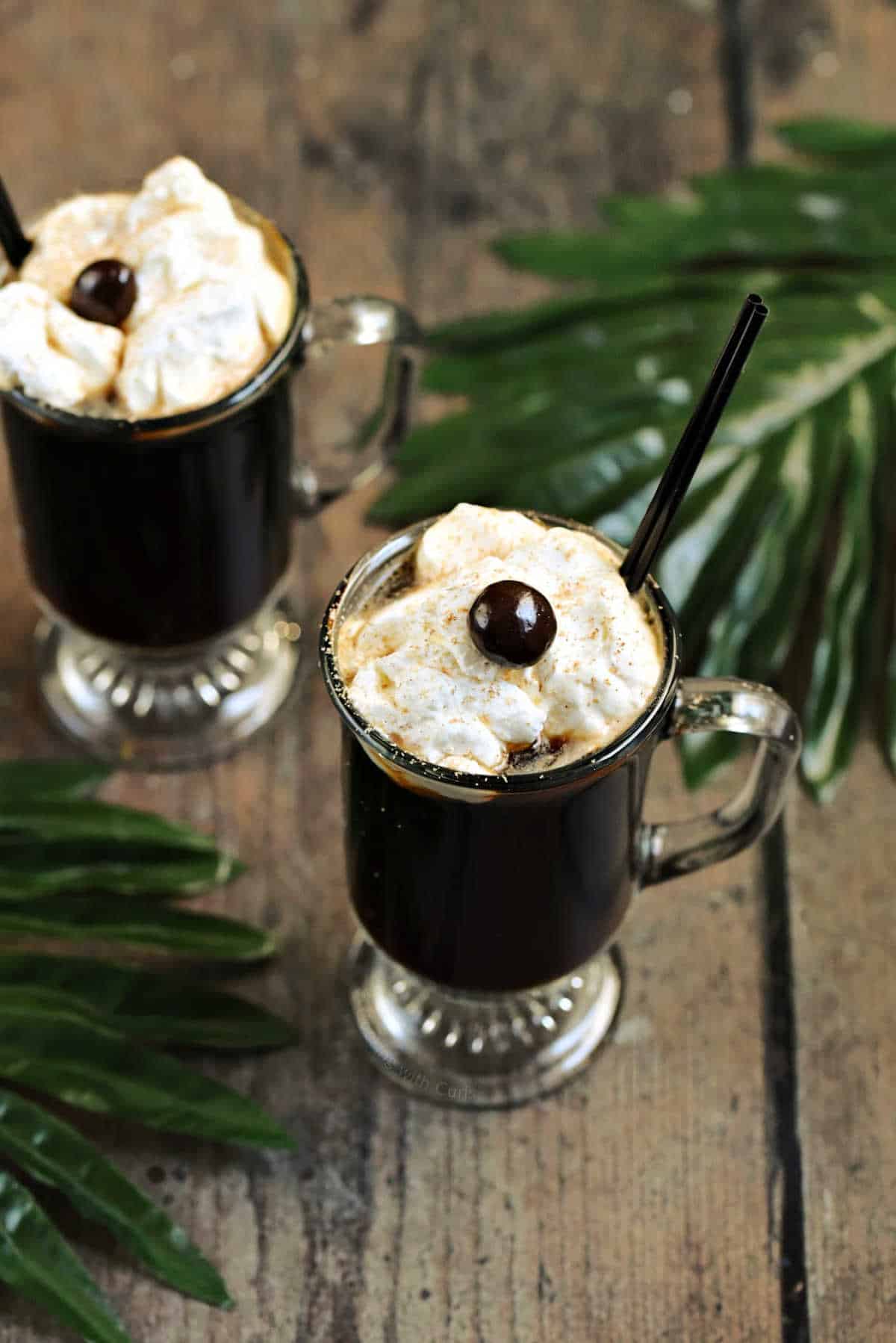 Two glass mugs filled with a coffee cocktail topped with whipped cream and a chocolate covered coffee bean.