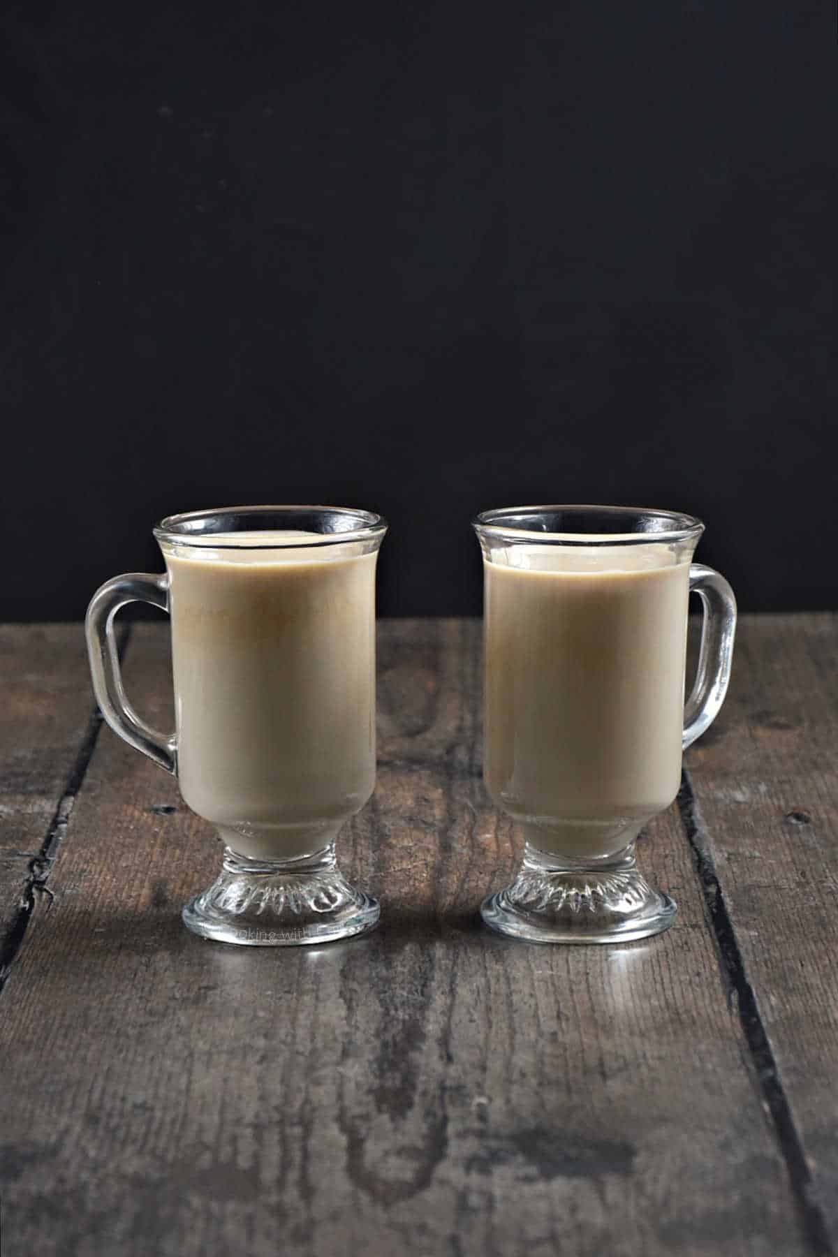 Two creamy coffee filled glass mugs.