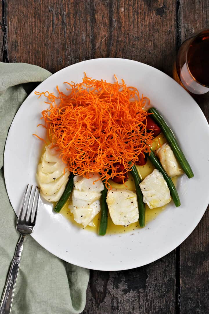 Butter Poached Sea Bass with green beans, peppers, and crispy sweet potato straws.