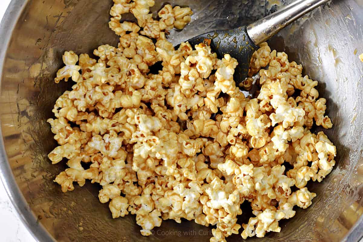 Popcorn tossed with honey, cinnamon, and flavorings in a mixing bowl.