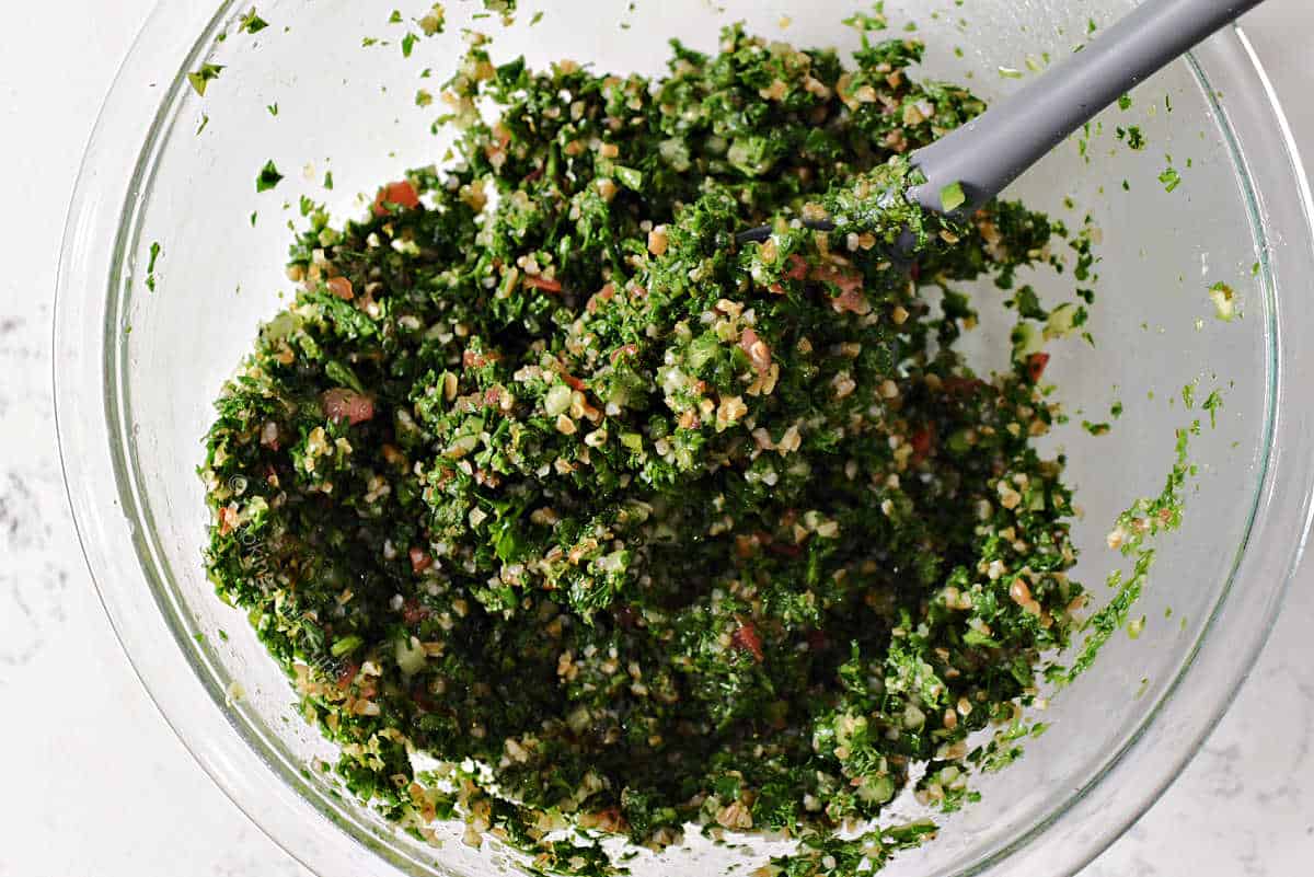 Tabbouleh ingredients mixed in glass bowl.