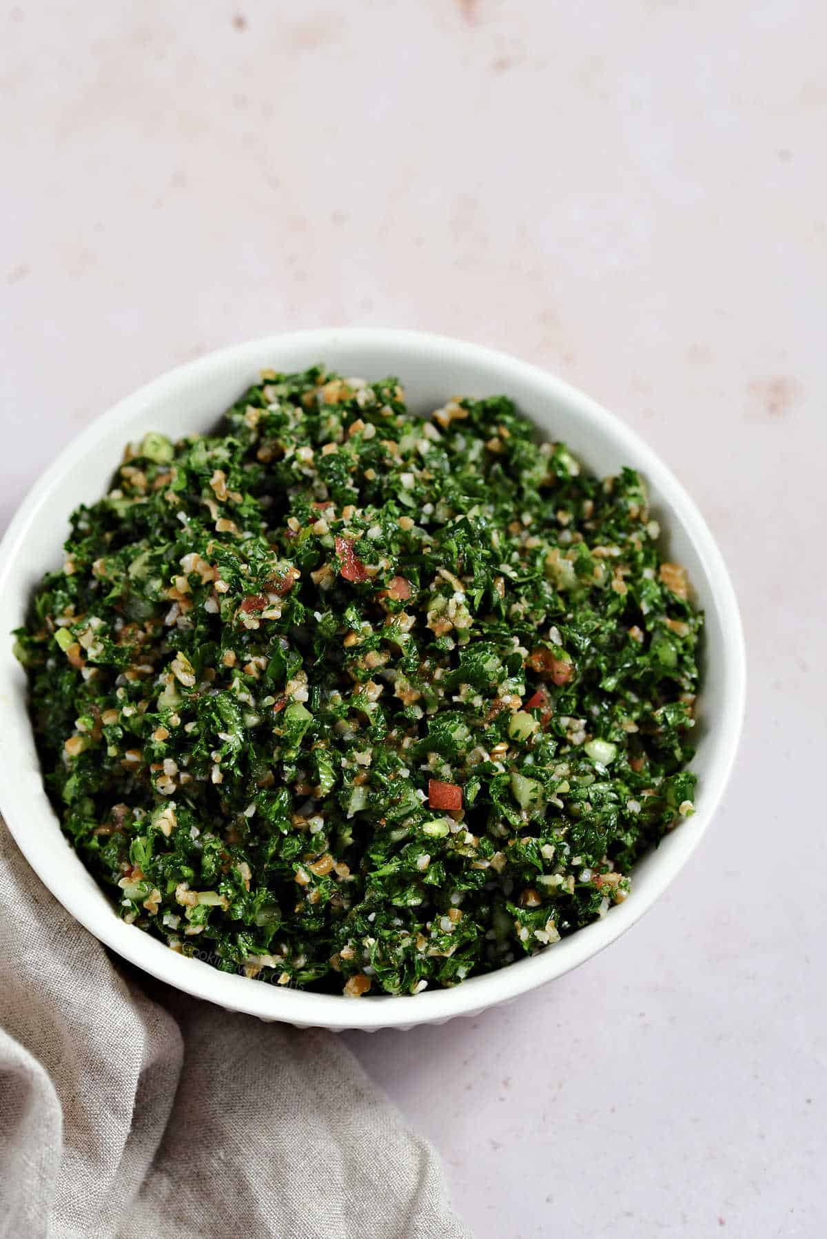 Fresh parsley, bulgar wheat, tomato, and cucumber chopped up and mixed in a bowl.