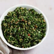 Fresh parsley, bulgar wheat, tomato, and cucumber chopped up and mixed in a bowl.