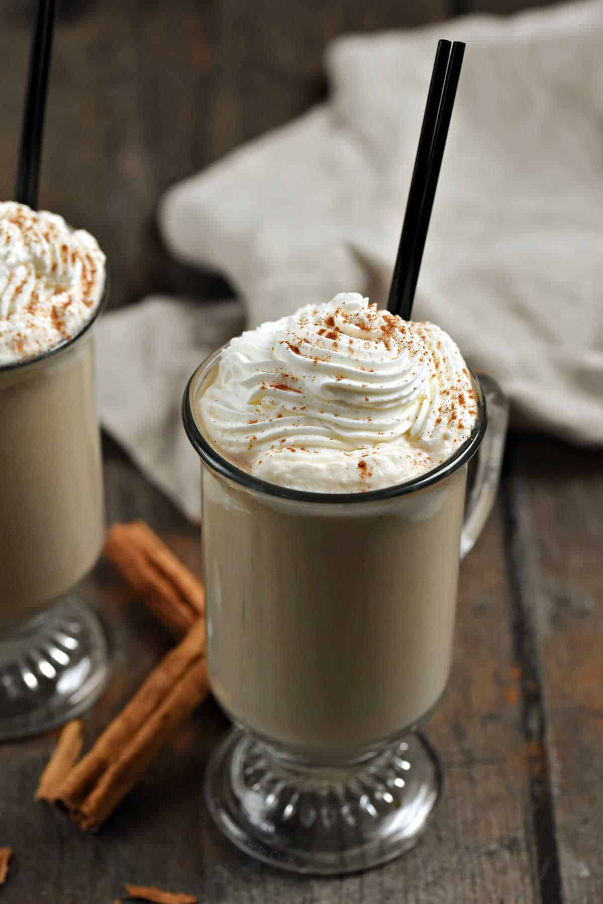 Two cinnamon latte cocktails in glass mugs topped with whipped cream and cinnamon.