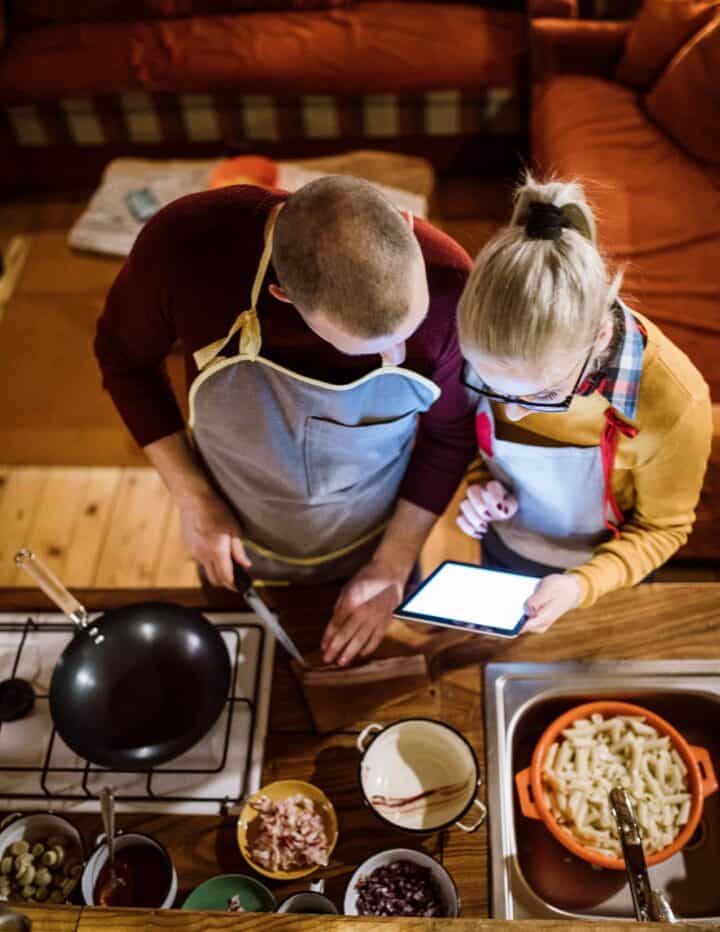 Couple cooking dinner while reading the recipe on their tablet.