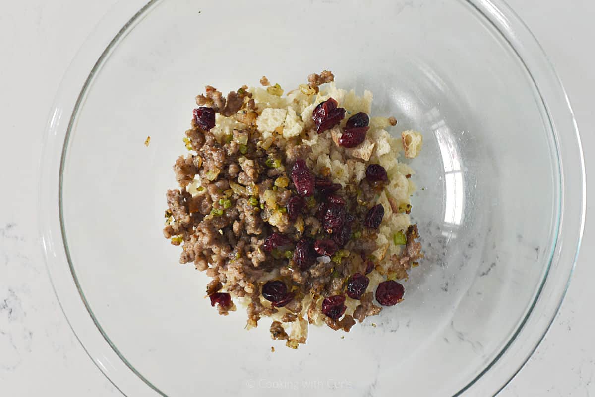 Bread cubes, sausage, cranberries, and herbs in a mixing bowl.