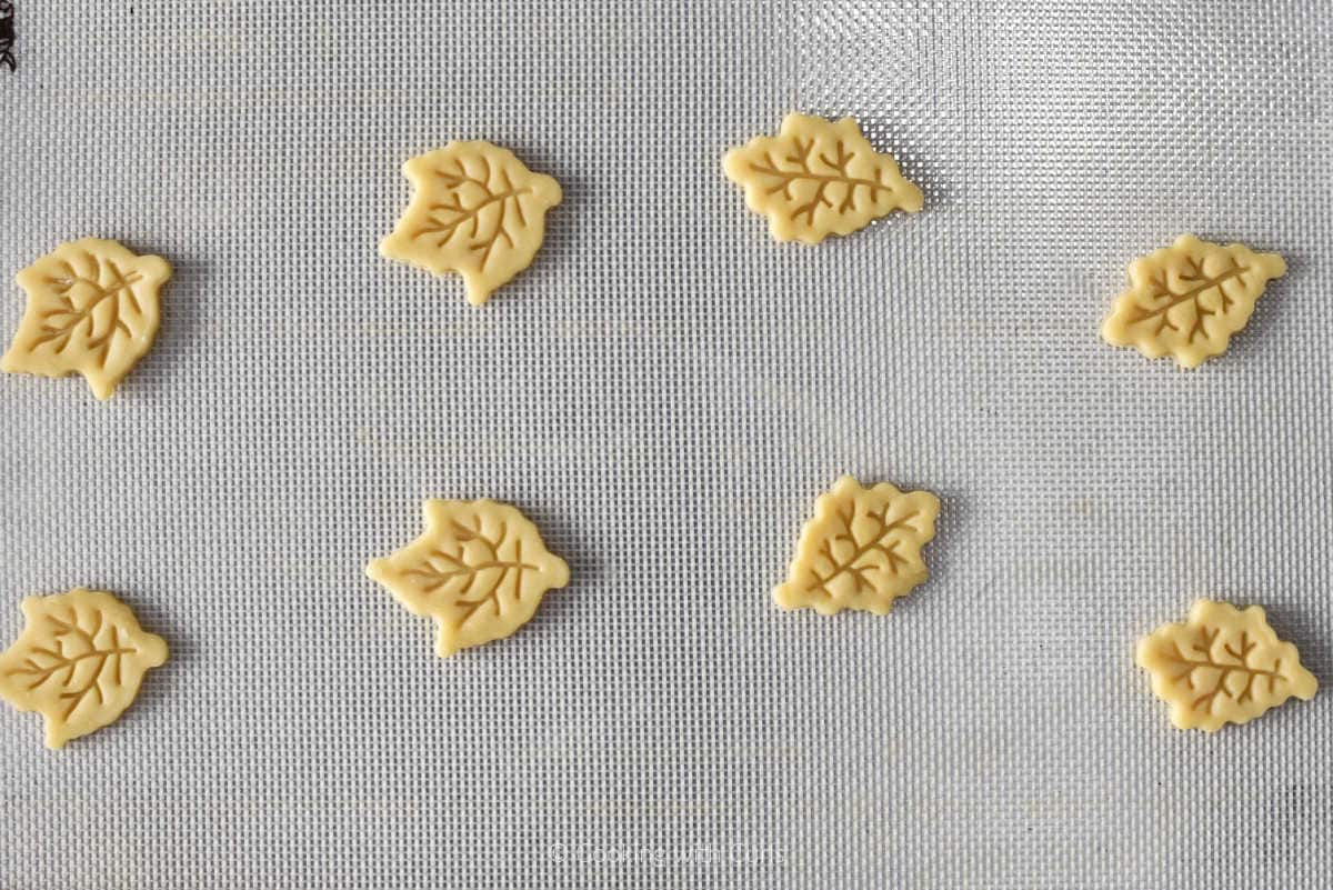 Eight leaf shaped pie crust mini cutouts on a baking sheet.