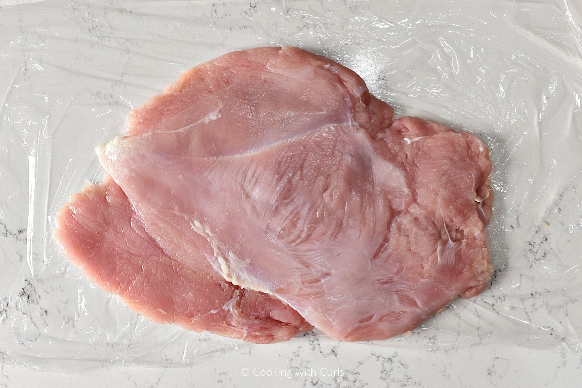 Flattened turkey breast on plastic wrap.