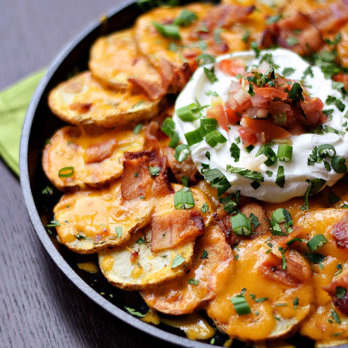 Sliced potatoes covered in melted cheese, bacon, sour cream, and salsa.