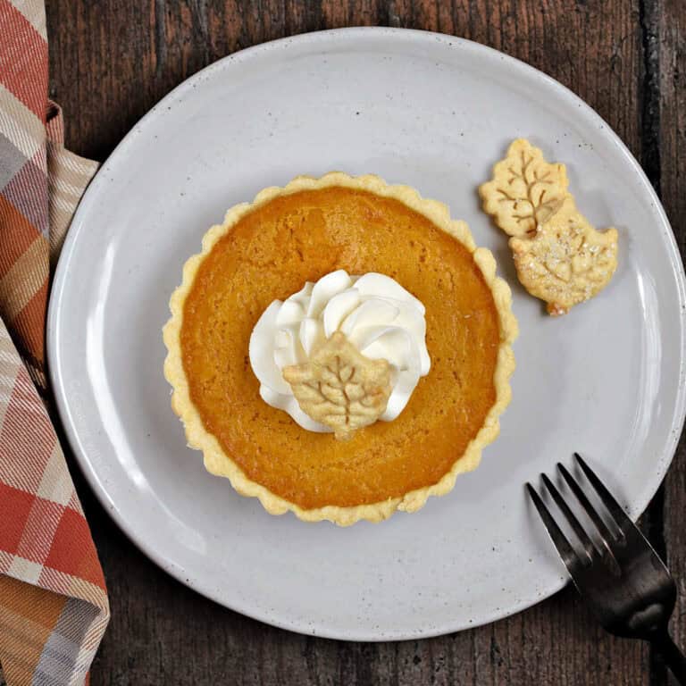 A mini pumpkin pie with whipped cream and pie crust leaf shaped cutouts.