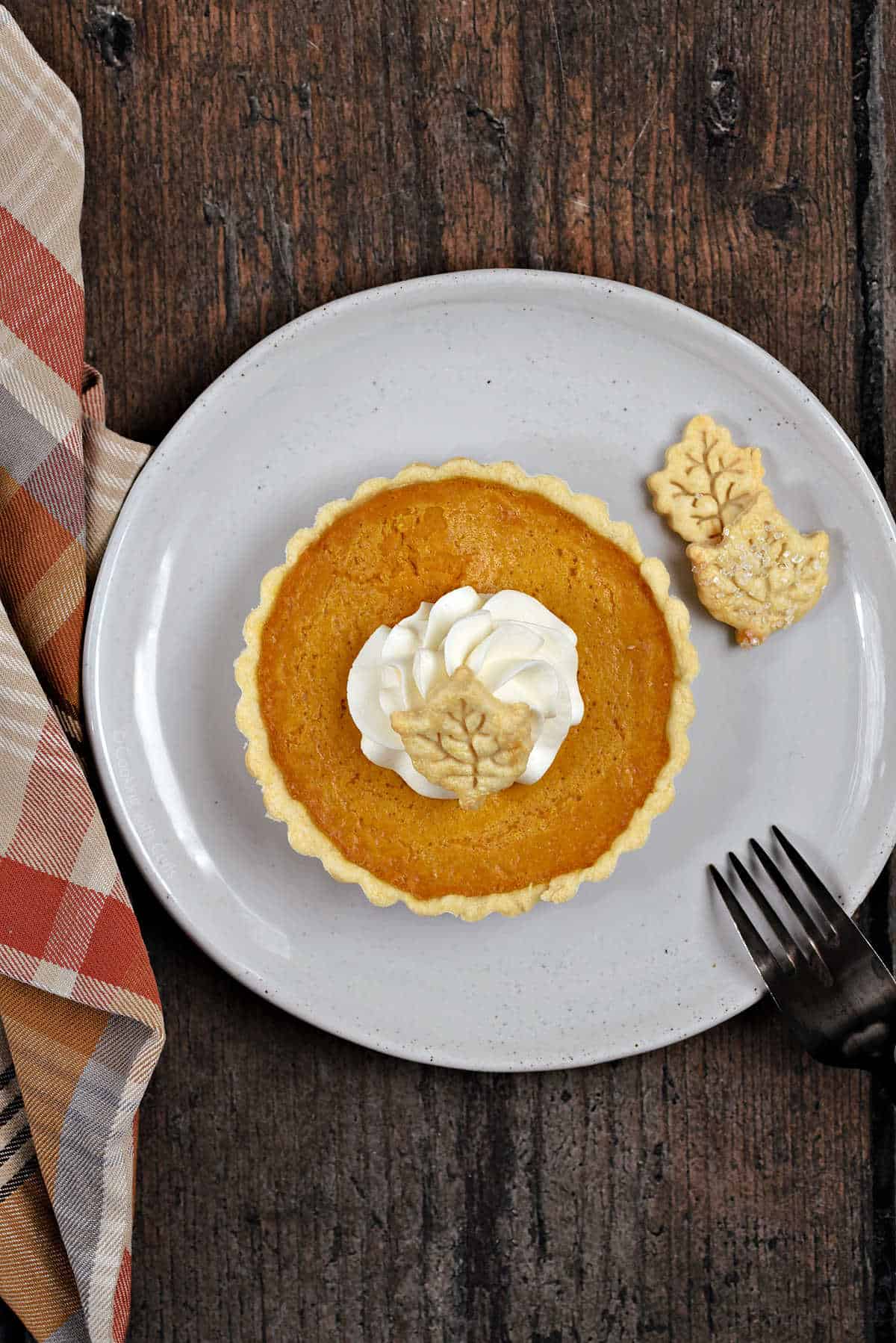 A mini pumpkin pie with whipped cream and pie crust leaf shaped cutouts.