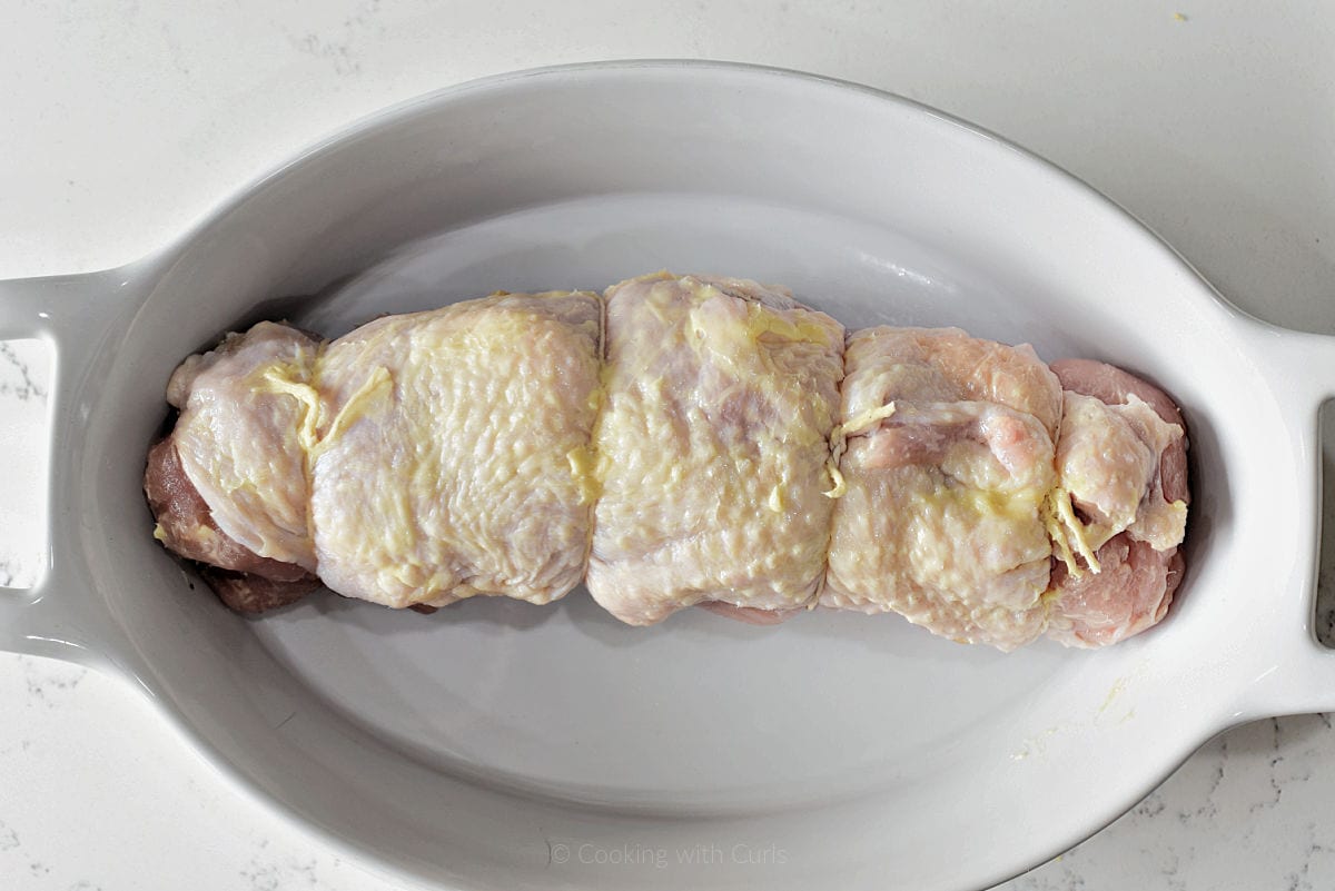 Raw, stuffed turkey roll wrapped with twine sitting in a baking dish.