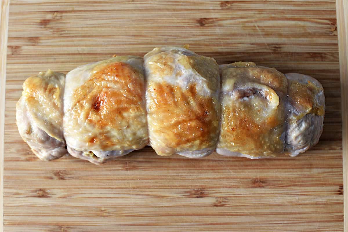 Roasted stuffed turkey breast on wood cutting board.