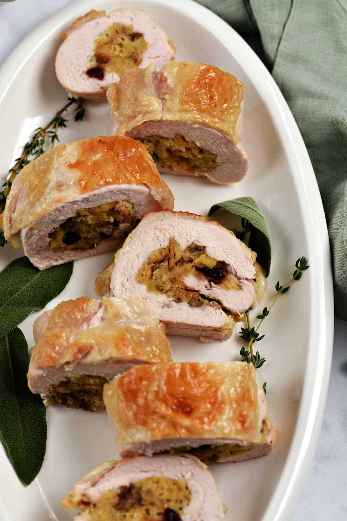 Seven slices of stuffed turkey breast with sausage and cranberries on a platter.