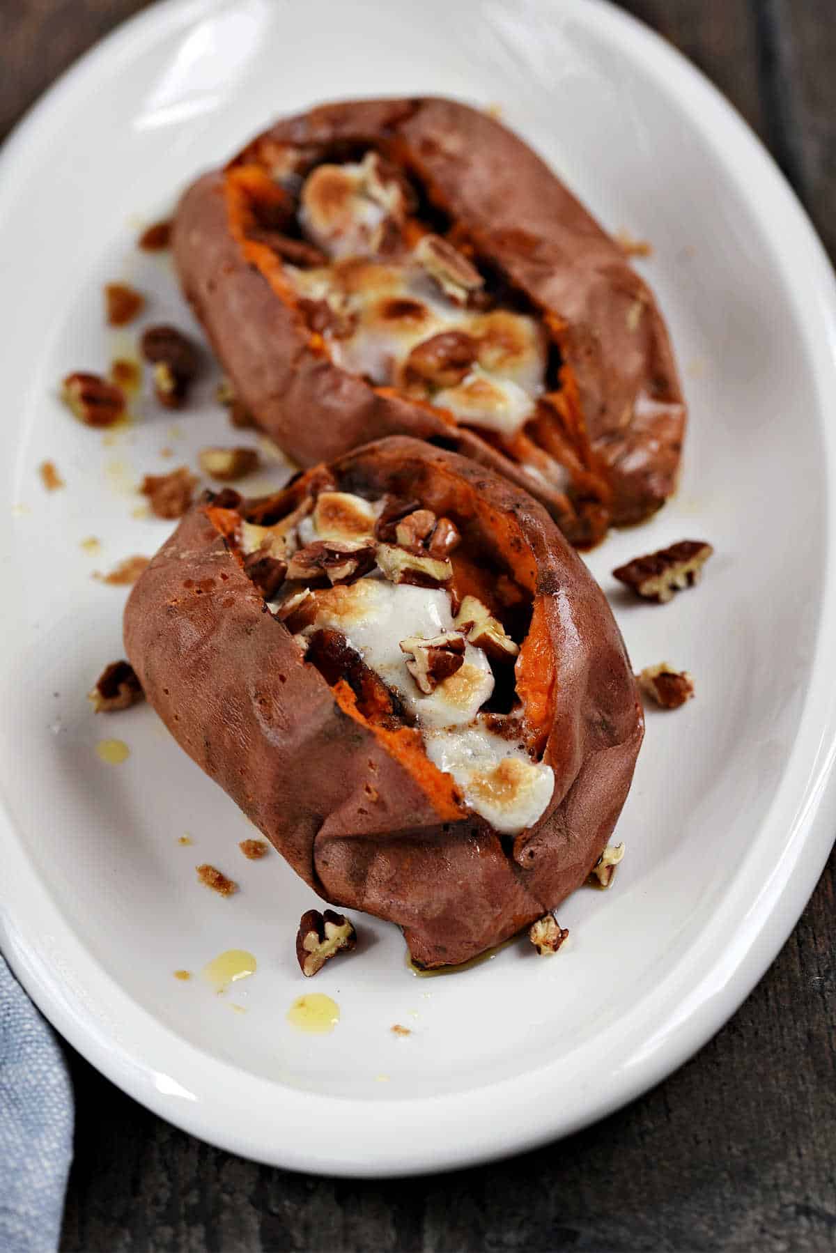 Two stuffed sweet potatoes topped with melted marshmallows and chopped pecans on a serving platter.