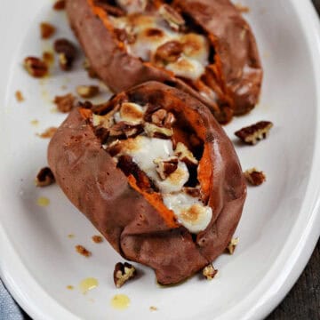 Two stuffed sweet potatoes topped with melted marshmallows and chopped pecans on a serving platter.