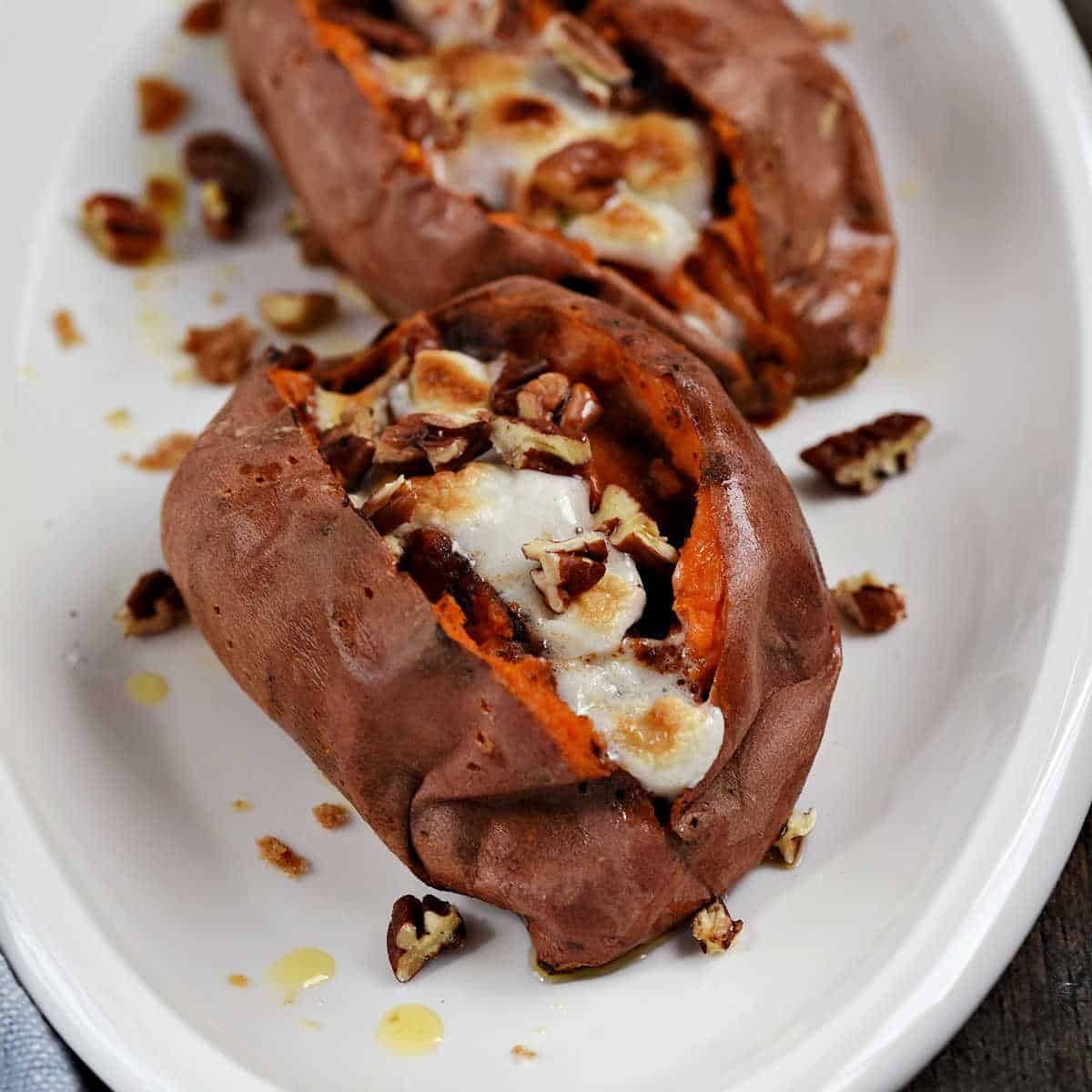 Two stuffed sweet potatoes topped with melted marshmallows and chopped pecans on a serving platter.