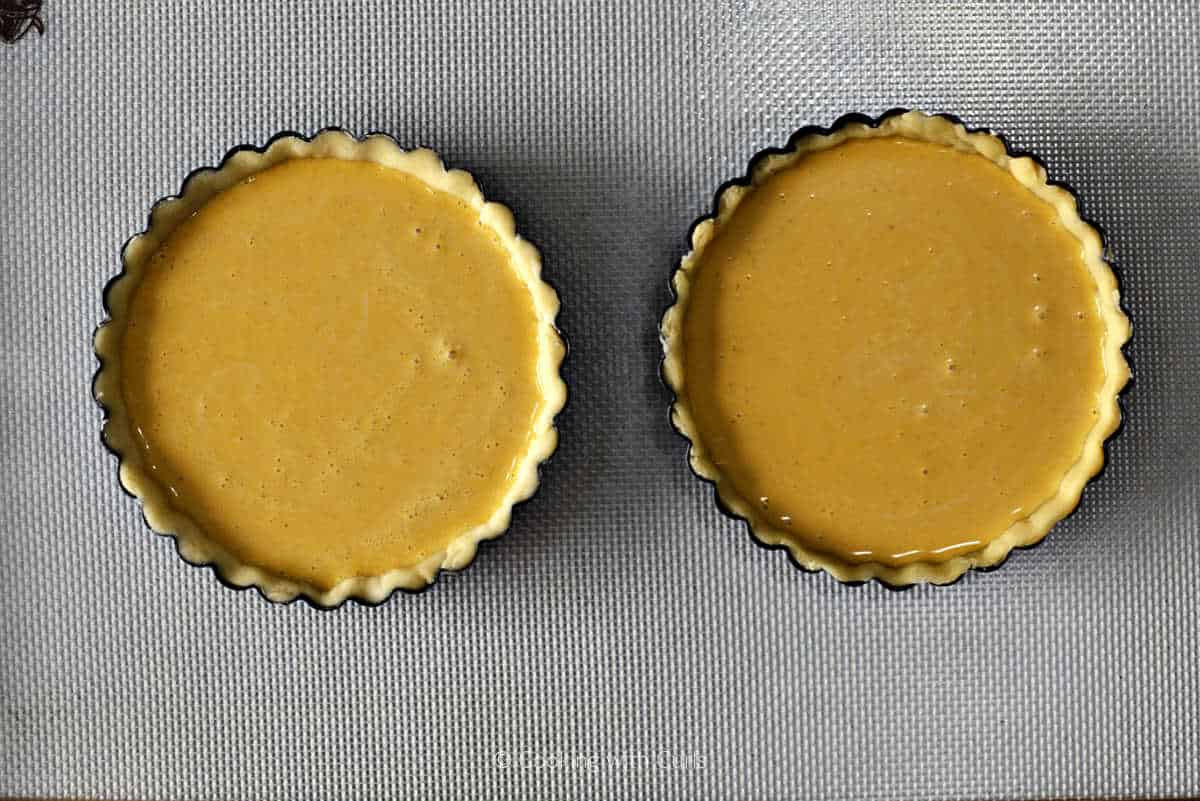 Two raw mini pumpkin pies on a baking sheet.