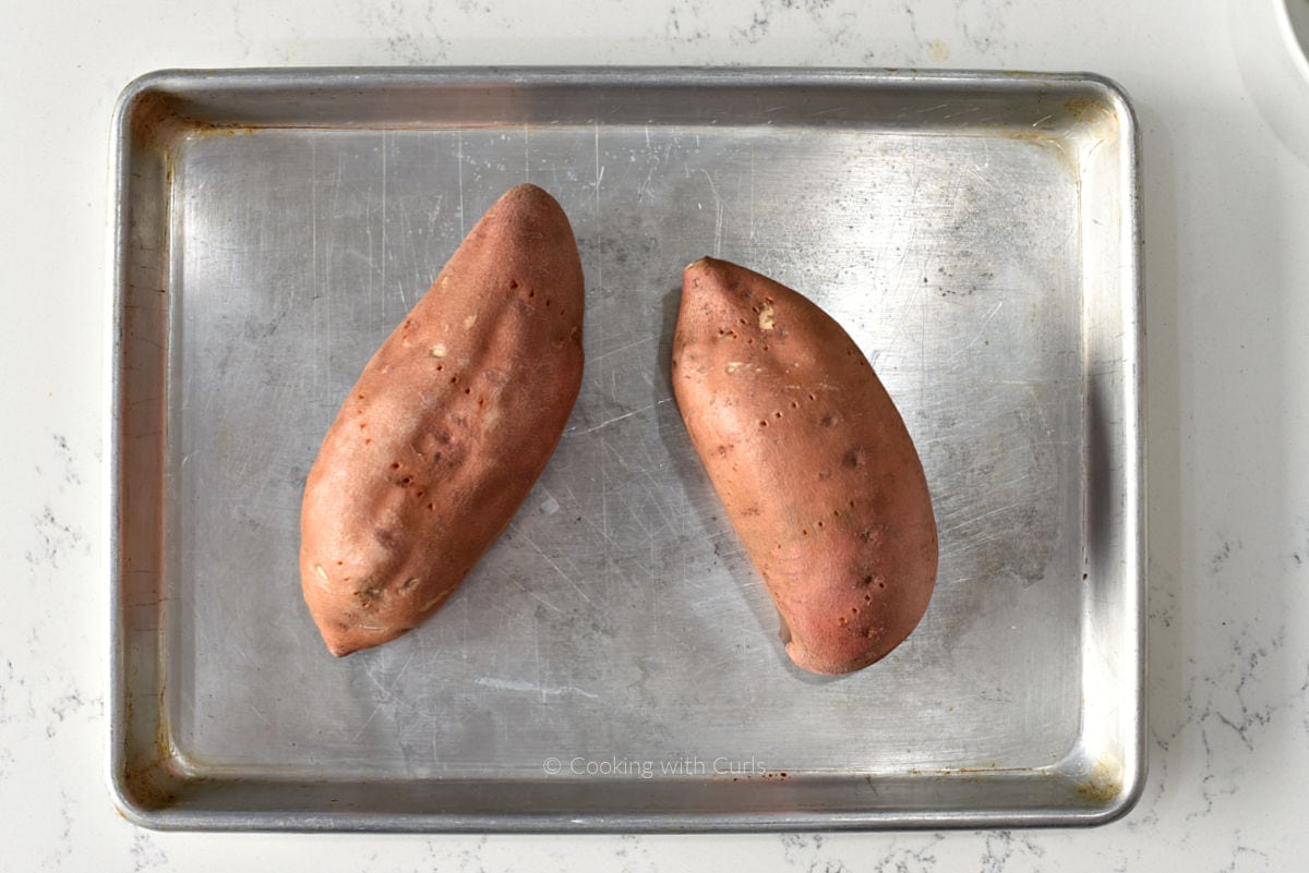 Two sweet potatoes on a small baking sheet.