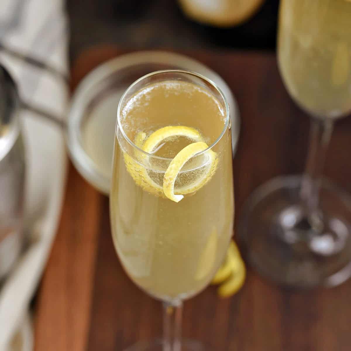 Bubbly yellow French 75 cocktail in a champagne flute with a lemon twist.