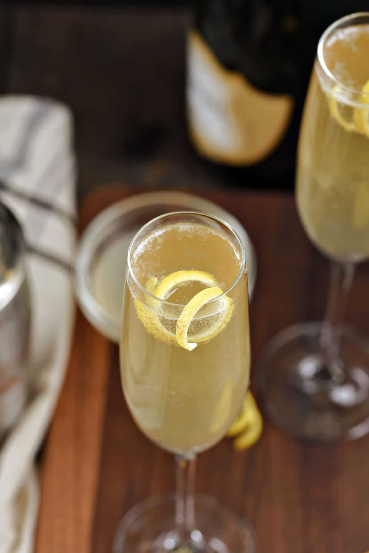 Bubbly yellow French 75 cocktail in a champagne flute with a lemon twist.