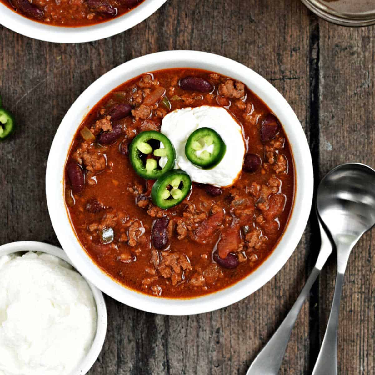 A bowl of chili topped with sour cream and sliced jalapeños.