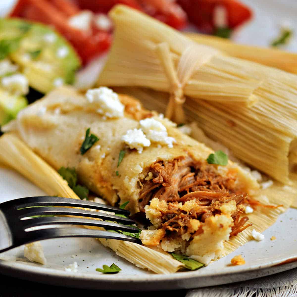 Red chile pork tamales on a plate with avocado slices.