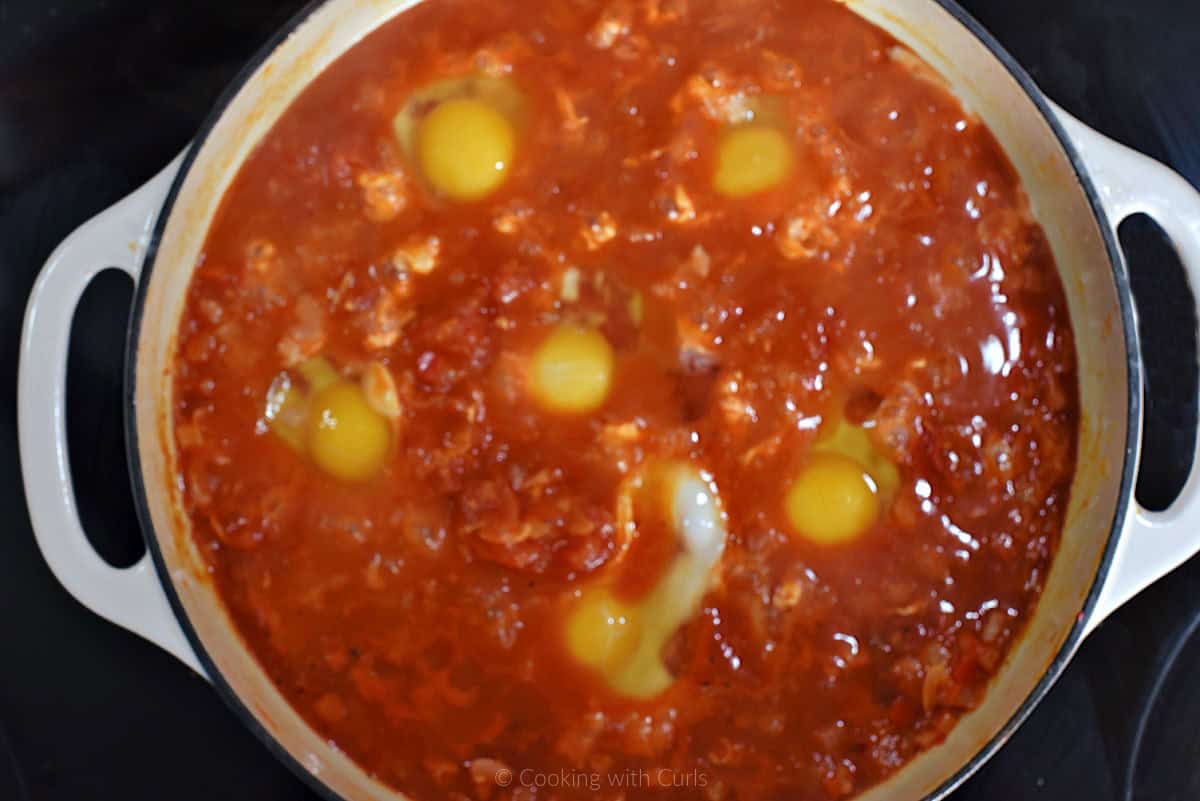 Six raw eggs in skillet with tomato sauce.