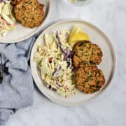 Two tuna patties on a plate with coleslaw and lemon wedges.
