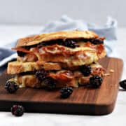 Two blackberry brie grilled cheese sandwiches stacked on a wood board.
