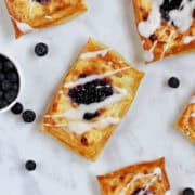 Four puff pastry danishes filled with cream cheese, blueberry preserves, and drizzled with glaze.