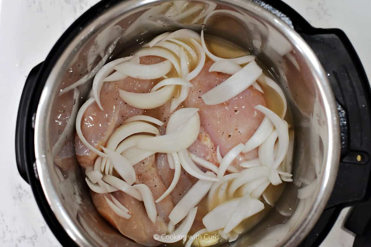 Chicken breasts, chicken broth, garlic, and onion slices in pressure cooker.