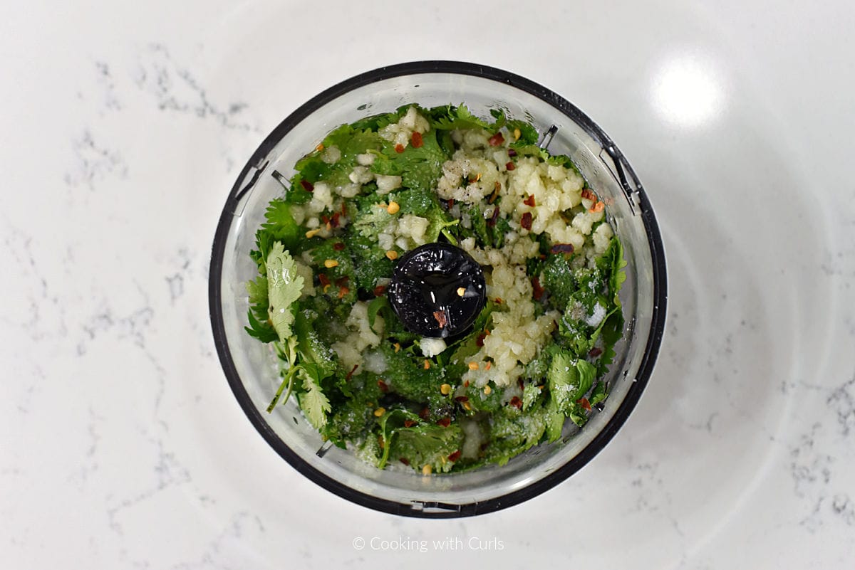 Cilantro, parsley, garlic, and chili flakes in food processor bowl.