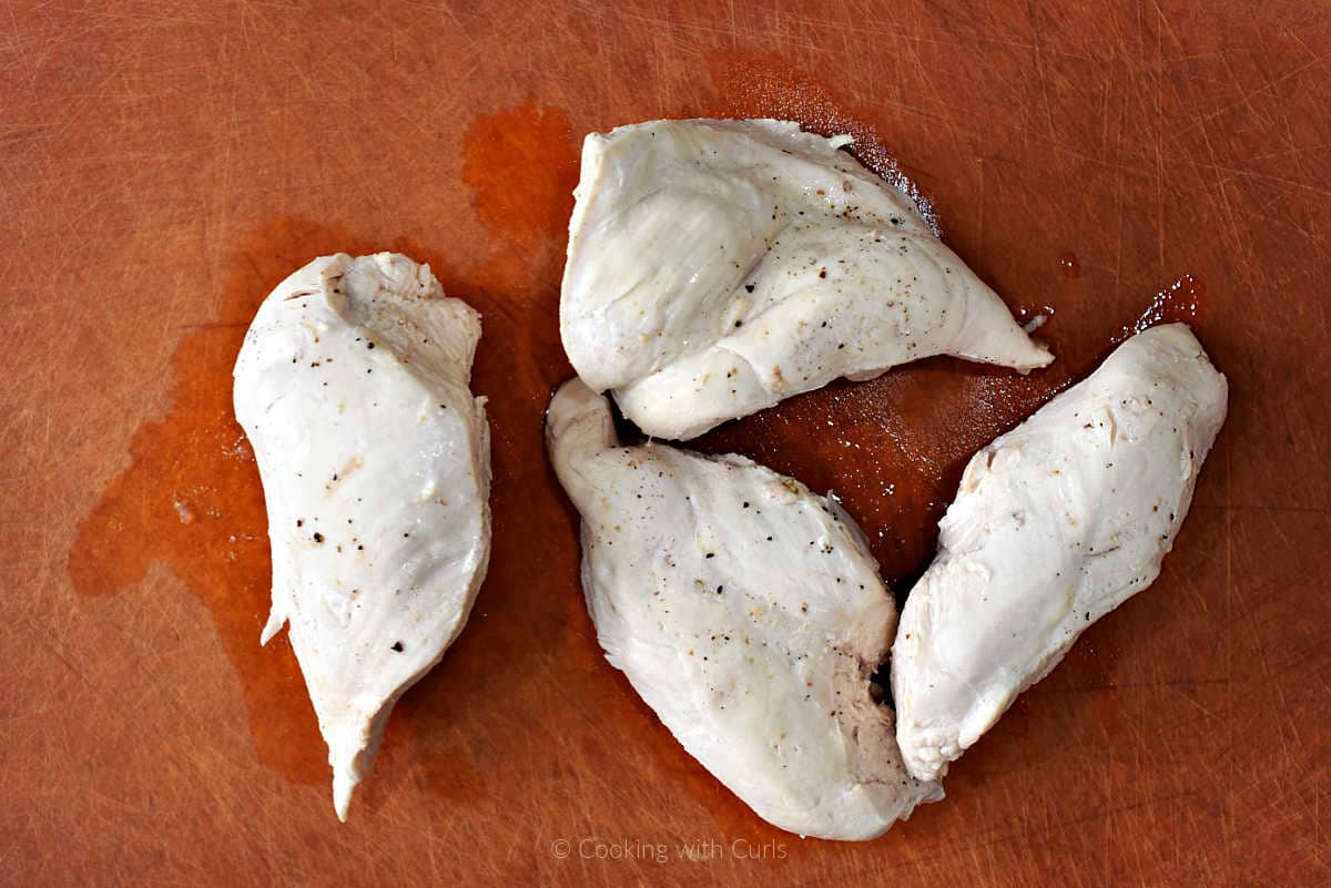 Four cooked chicken breasts on cutting board.