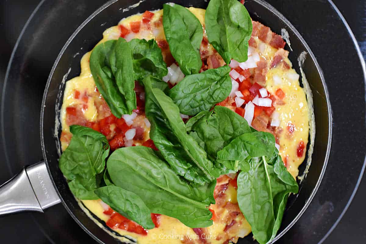 Fresh spinach leaves over eggs, peppers, and onion in small skillet.
