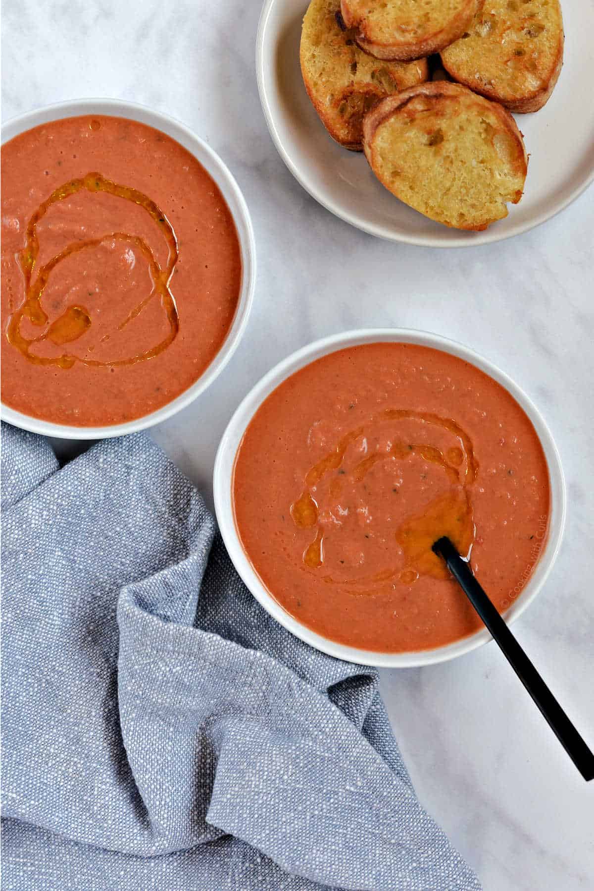 Two bowls of bright orange soup drizzled with olive oil, with a plate of crostini on the side.